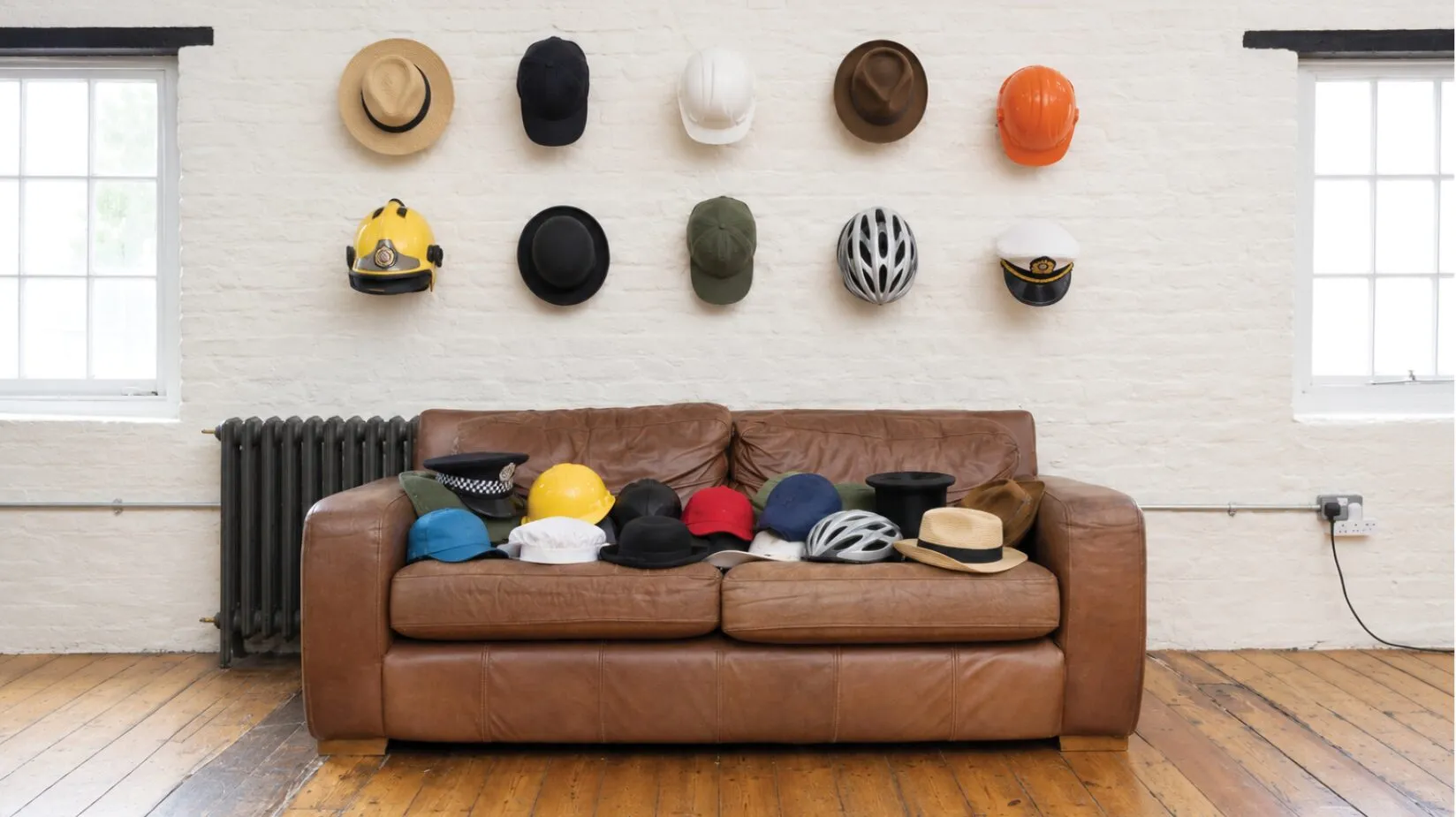 A leather sofa in the Curation studio with a row of hats arranged on the wall above