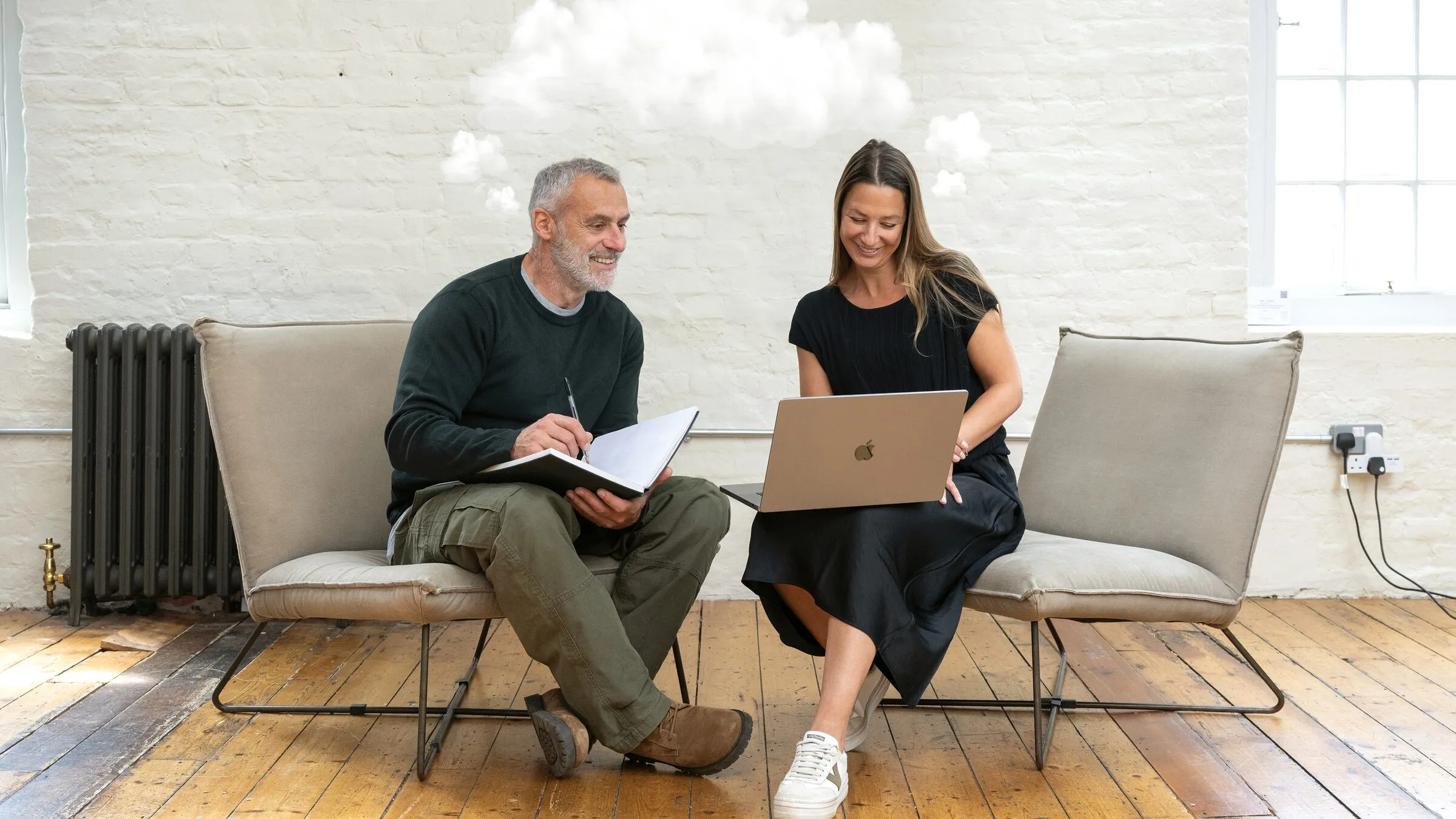 Two members of the Curation team working together on a sofa, one with a notebook and one with a laptop